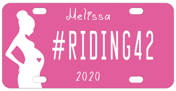 Pink Background with silhouette of a pregnant woman with a pink heart in her belly. Our sample reads #riding42 in the center with name on top and year on bottom. You can personalize with any text in all three areas