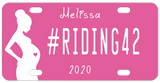 Pink Background with silhouette of a pregnant woman with a pink heart in her belly. Our sample reads #riding42 in the center with name on top and year on bottom. You can personalize with any text in all three areas