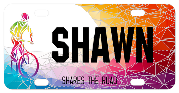 Fractured colors appearing like diamonds or stained glass pieces is the backdrop to a bike rider on these cool custom share the road license plates